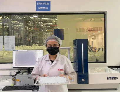 Angel Loh, Chemikerin bei Hiroyuki, mit rPET-Pelletproben, die mit dem Inspektionssystem geprüft werden, Bild: Sikora Angel Loh, Chemikerin bei Hiroyuki, mit rPET-Pelletproben, die mit dem Inspektionssystem von Sikora geprüft werden